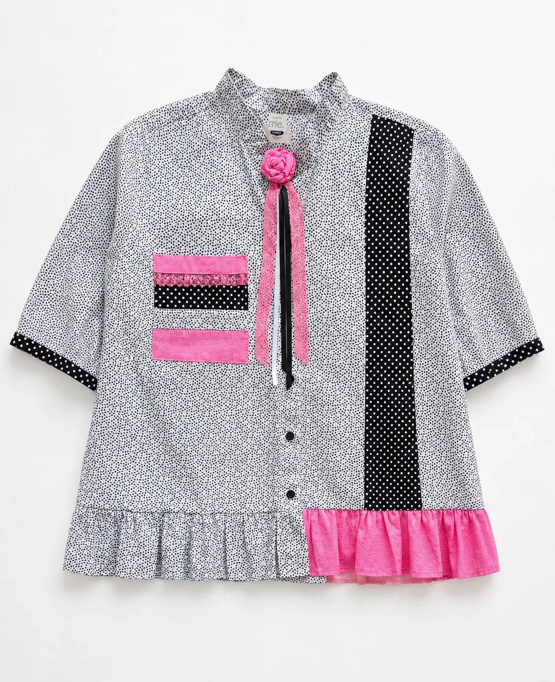 Dolly — black and white micro-print blouse with polka dot panel, pink accents, ruffled hem and pink flower at neckline, flat lay